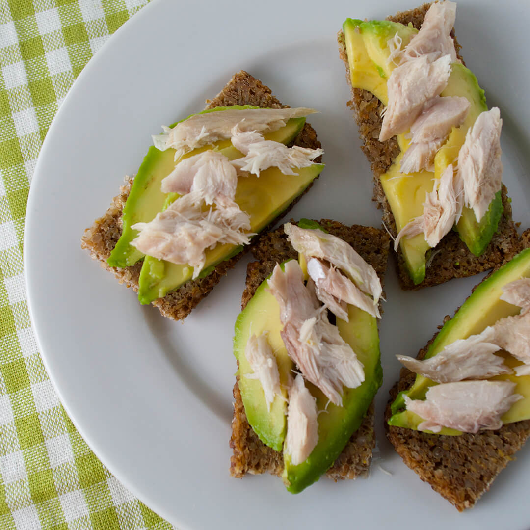 A slice of rye bread cut into quarters and topped with avocado and mackerel